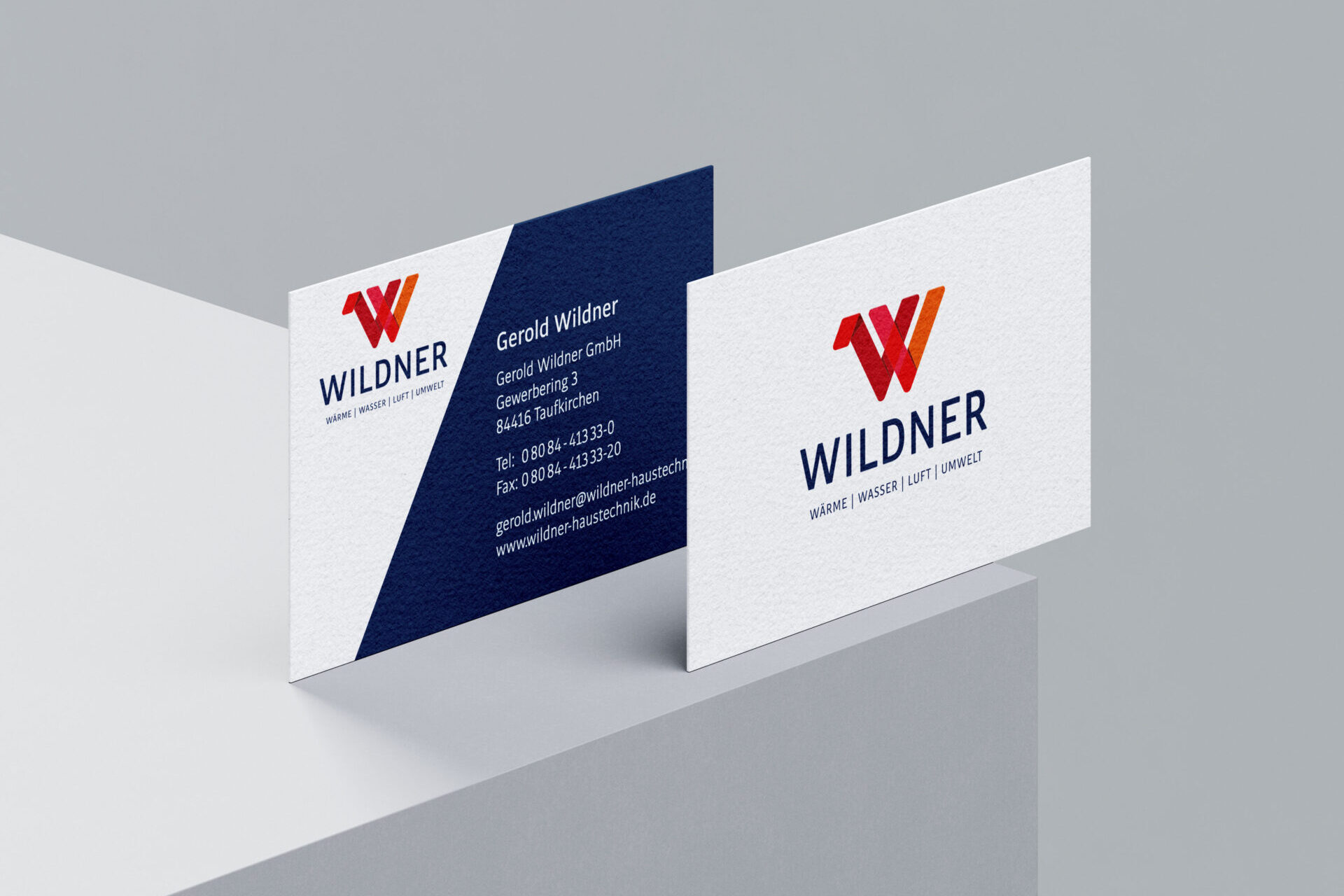 Zwei Visitenkarten zeigen das Wildner Haustechnik-Logo mit einem fetten roten W, den Firmennamen und die Kontaktangaben. Eine Karte zeigt das Logo und den Slogan, auf der anderen sind Name, Adresse, Telefon, Fax und E-Mail einer Person aufgeführt.