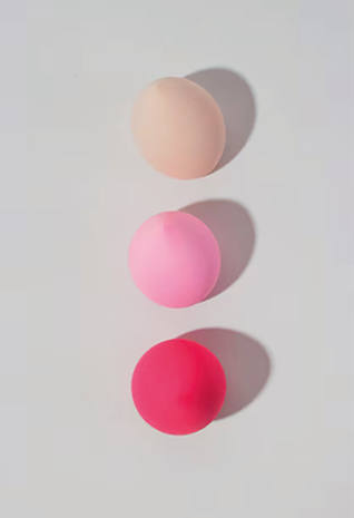 3 Kugeln_jv3dBN 1 Drei runde Make-up-Schwämme in den Farben Beige, Pink und Rot sind vertikal auf einem hellen Hintergrund angeordnet und werfen jeweils einen Schatten nach rechts - perfekt für eine werbeagentur Karlsruhe, die eine auffällige Produktdarstellung sucht.