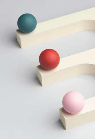 Kugeln auf Holz_aVRCWJ 1 Drei farbige Kugeln - zartblau, rot und rosa - sind einzeln auf cremefarbenen, geschwungenen Plattformen platziert und bilden ein Schleifenmuster vor einem hellgrauen Hintergrund. Perfekt für ein modernes Gestaltungskonzept der werbeagentur Karlsruhe.