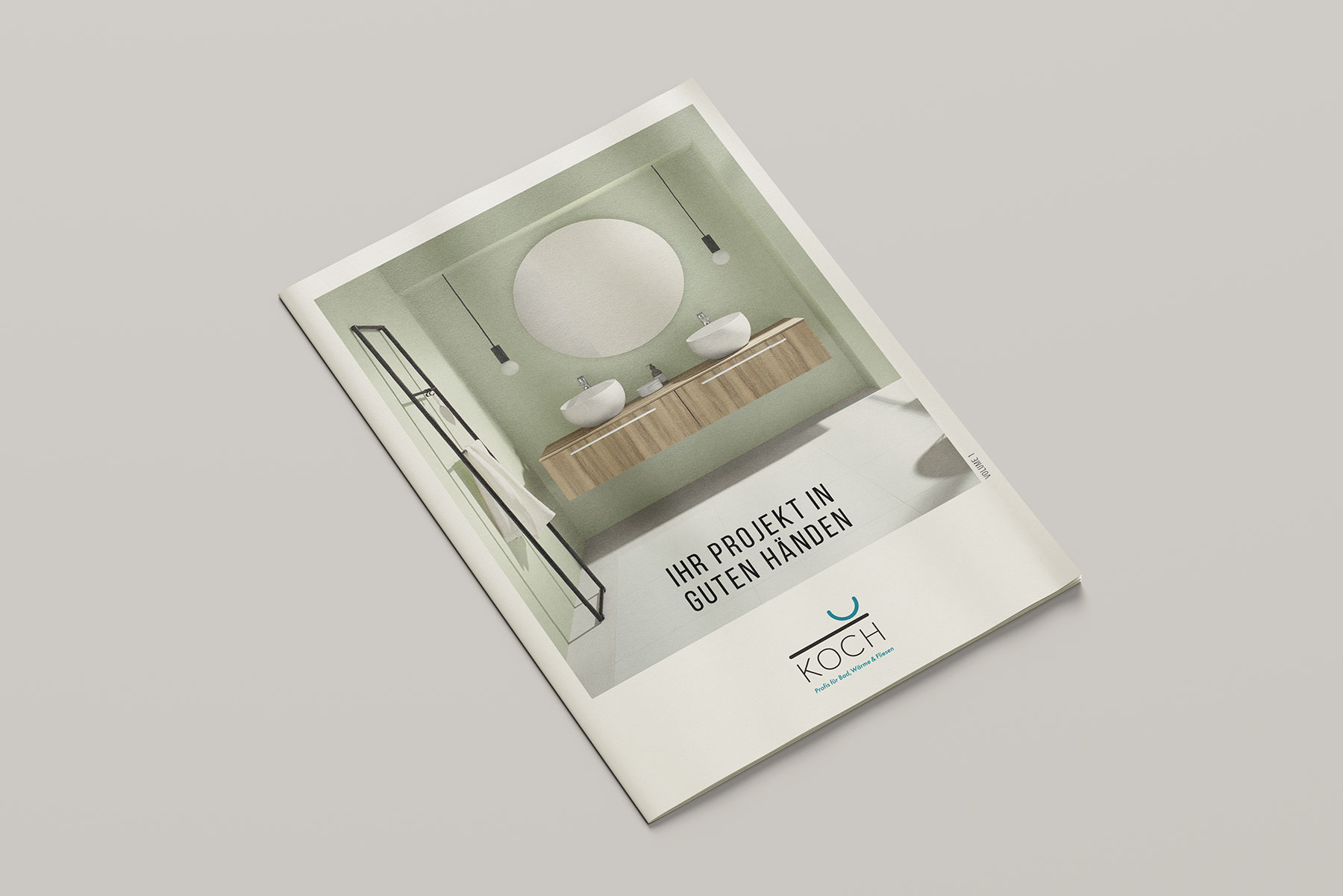 Eine Brosch&uuml;re mit dem Titelbild eines modernen Badezimmers mit rundem Spiegel, zwei Waschbecken, H&auml;ngeleuchten und Holzschr&auml;nken. Der Text lautet "IHR PROJEKT IN GUTEN H&Auml;NDEN" und enth&auml;lt am unteren Rand das Logo der Firma KOCH.